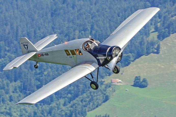 Der Co-Pilot winkt den Zuschauern der OldtimAIR Flugparade 2022 in Stanserhorn (Schweiz) freundlich aus dem offenen Cockpit der „JUNKERS F13“ zu. Eine großartige Air-to-Air-Schrägaufnahme des kleinen Passagierflugzeugs, welches in der Zeit nach dem Ersten Weltkrieg den Beginn des zivilen Luftverkehrs einläutete.© VJL /  Foto: Ugo Vincenzi  
